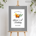 A personalized black and white striped welcome sign on a wooden easel, featuring a cocktail illustration and the text 'Welcome to Steven's 40th Birthday' with a date.