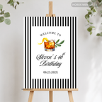 A personalized black and white striped welcome sign on a wooden easel, featuring a cocktail illustration and the text 'Welcome to Steven's 40th Birthday' with a date.
